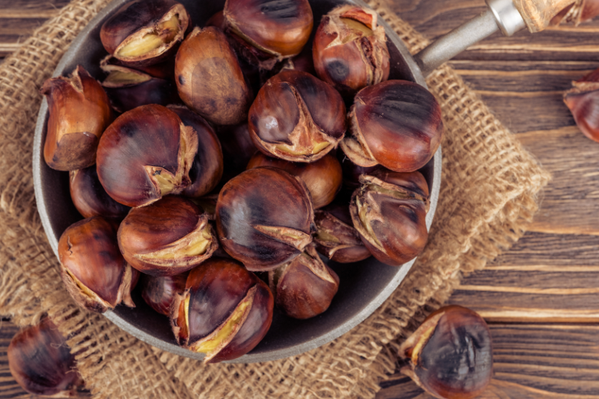 KI generiert: Eine Pfanne mit gerösteten Kastanien auf einem Holztisch.