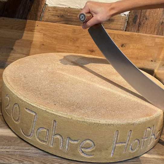 KI generiert: Ein großer Käselaib, darauf die Inschrift: "20 Jahre Hofb."