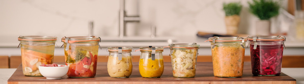 KI generiert: Verschiedene Einmachgläser mit fermentiertem Gemüse in einer Küche auf einem Holzbrett.