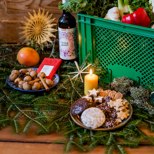 KI generiert: Ein Weihnachtstisch mit Keksen, Nüssen, Gemüse, einer Kerze und einer grünen Kiste.