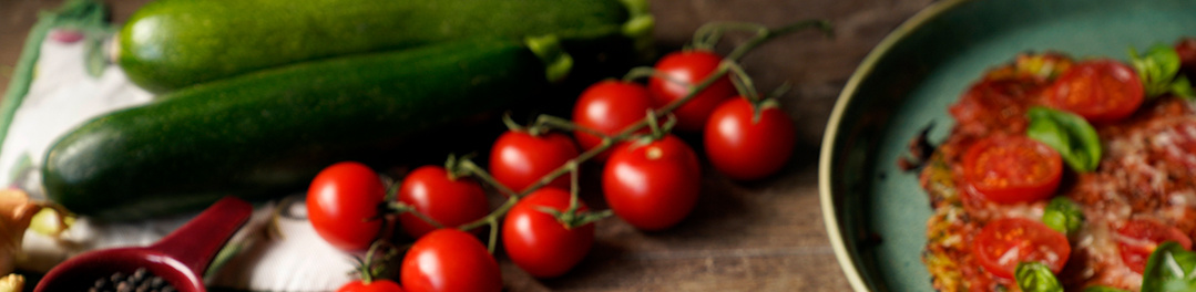 KI generiert: Zucchini, Tomatenrispe und ein Teller mit einem Gericht garnieren das Bild.