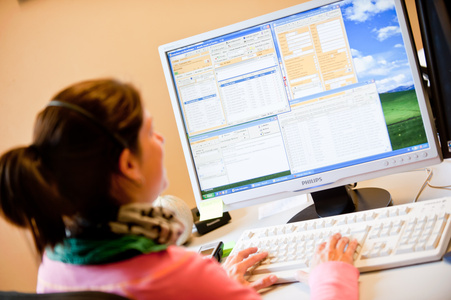 KI generiert: Eine Person sitzt an einem Schreibtisch und arbeitet am Computer, wobei auf dem Monitor verschiedene geöffnete Fenster zu sehen sind. Das Bild zeigt eine Büroszene, in der die Person Informationen auf dem Bildschirm betrachtet.