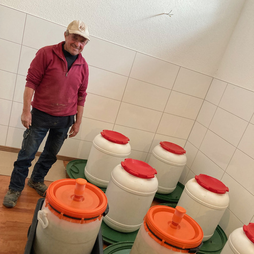 KI generiert: Ein Mann steht neben mehreren weißen Behältern mit roten Deckeln in einem gefliesten Raum.