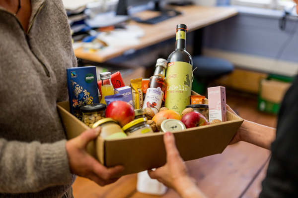 KI generiert: Zwei Personen halten einen Geschenkkorb mit Lebensmitteln, Getränken und Kosmetikprodukten.